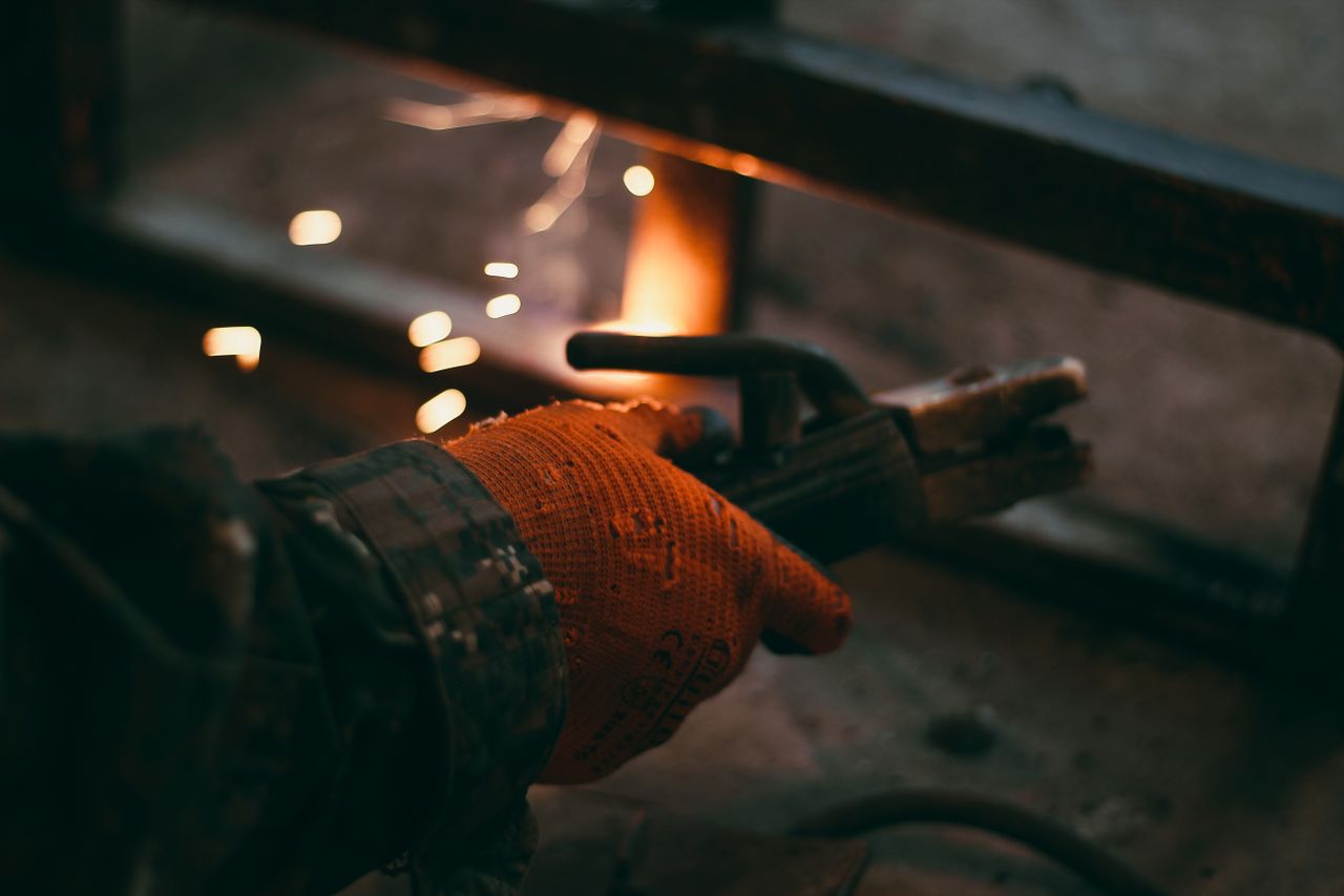 Detailed shot of a gloved hand holding an electrode holder during welding, sparks flying.